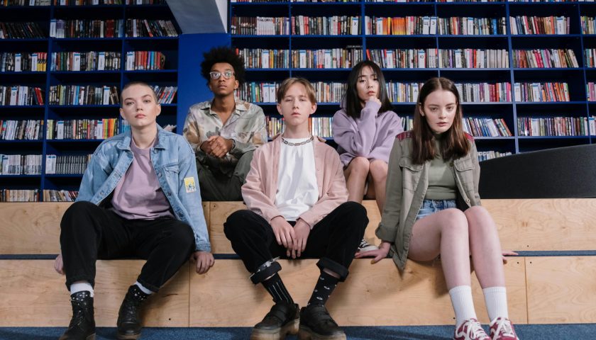 A group of diverse teenagers sitting in a library, showcasing youth diversity and style.