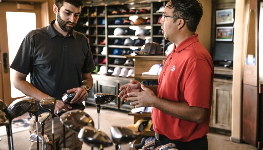 Customer receiving expert advice from salesman on golf equipment in a store.